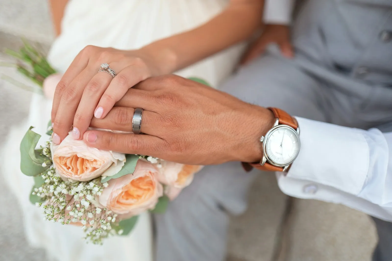 Manos de la pareja sosteniendo el ramo, con las argollas puestas